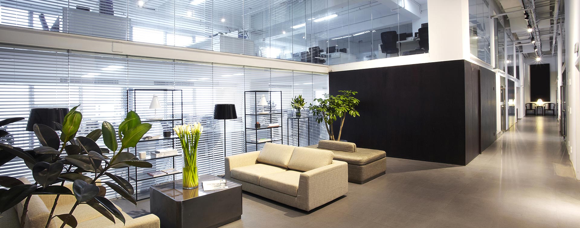 Modern office lounge area with sofas and plants among glass infrastructure.