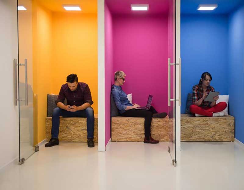 Yellow, pink and blue cubicles side-by-side with employees in each one working in private