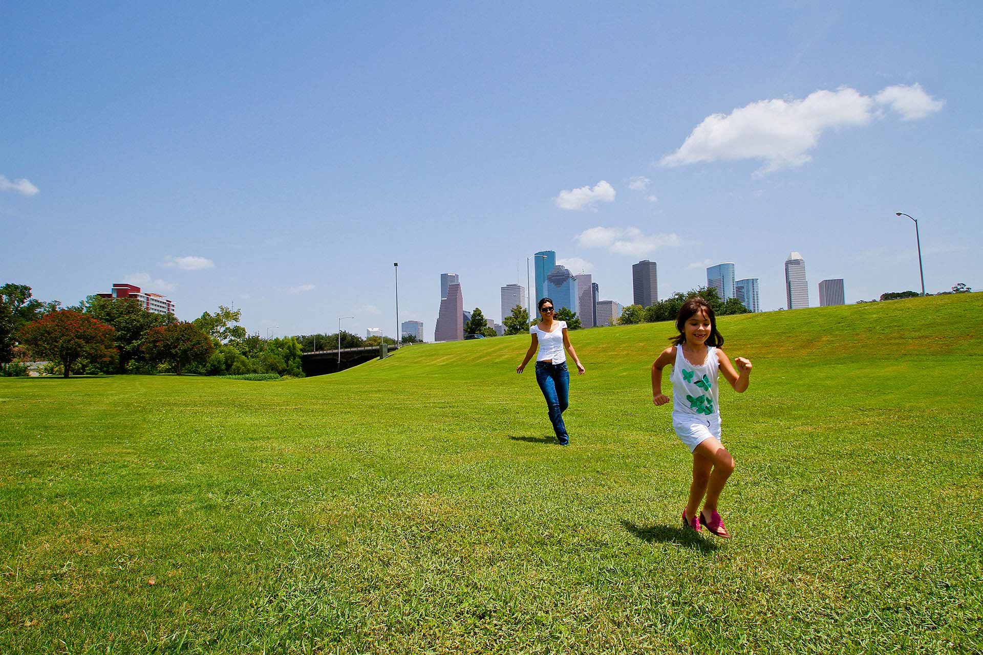 Mum chasing daughter in a field with a backdrop of the city