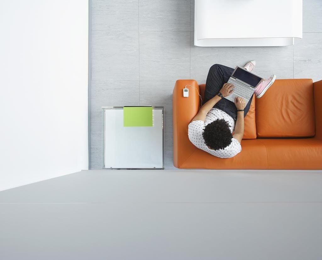 Employee working on laptop while listening to ipod and sitting on brown sofa in fresh, clean room