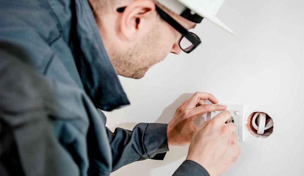 Male sub contractor installing plug socket into white wall